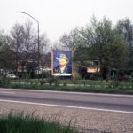 Zelfportret met grijze vilthoed als billboard langs de weg